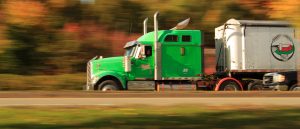 Green semi-truck on the road and a blurred fall foliage background